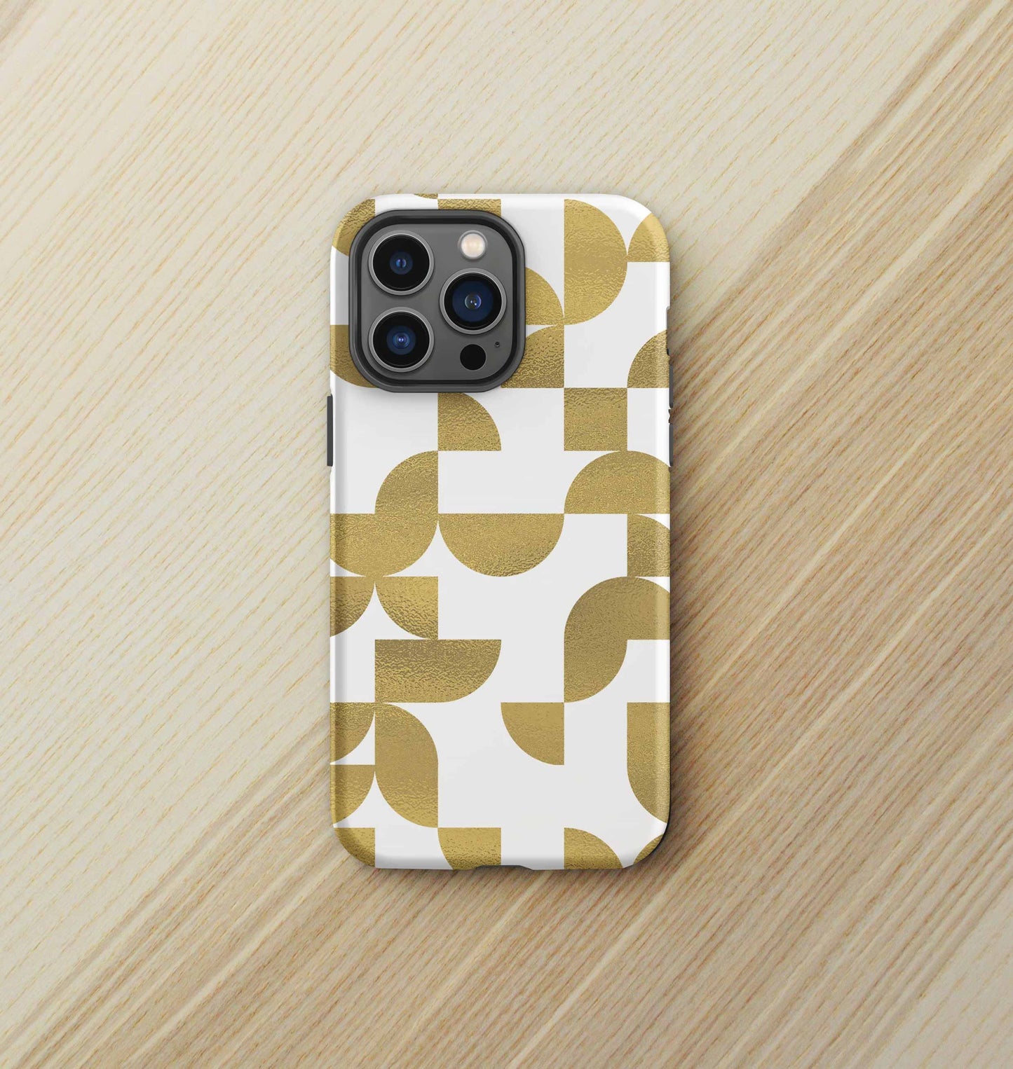 Front view of iPhone tough case in Geometria I gold design on a birch desktop