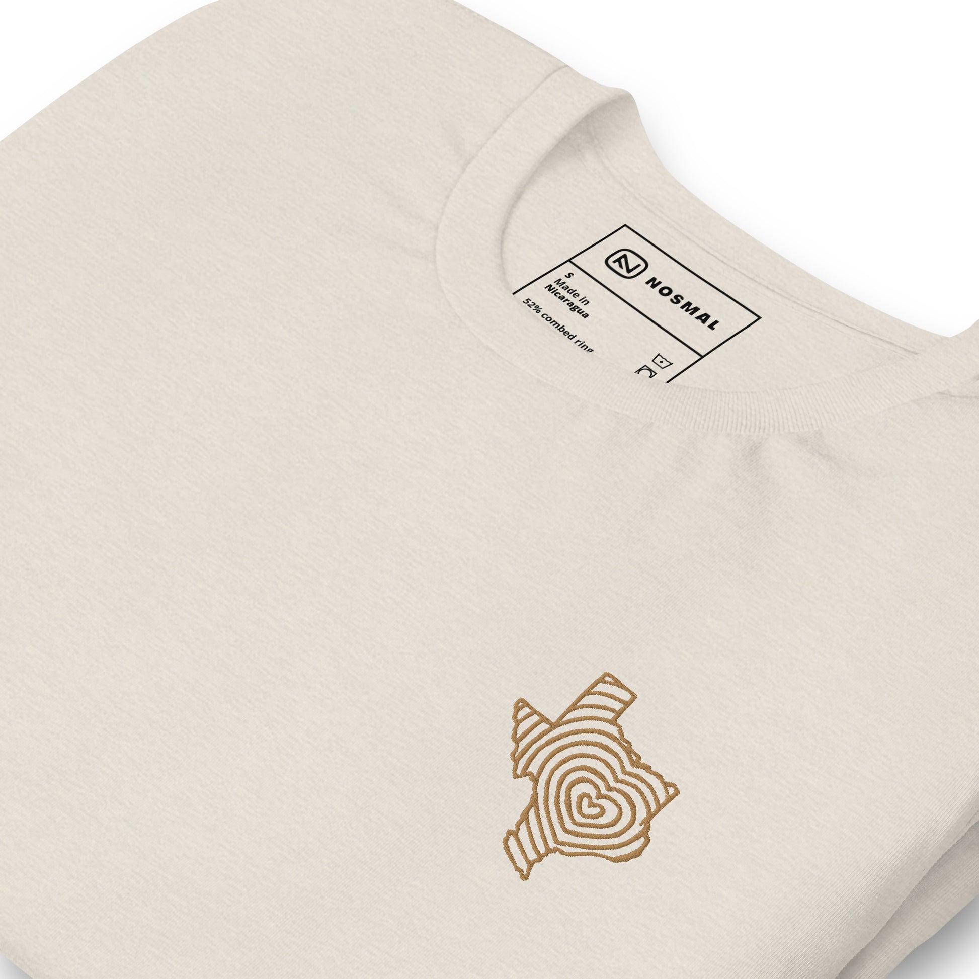 Angled close up shot of heartbeat of texas gold embroidered design on heather dust unisex t-shirt.