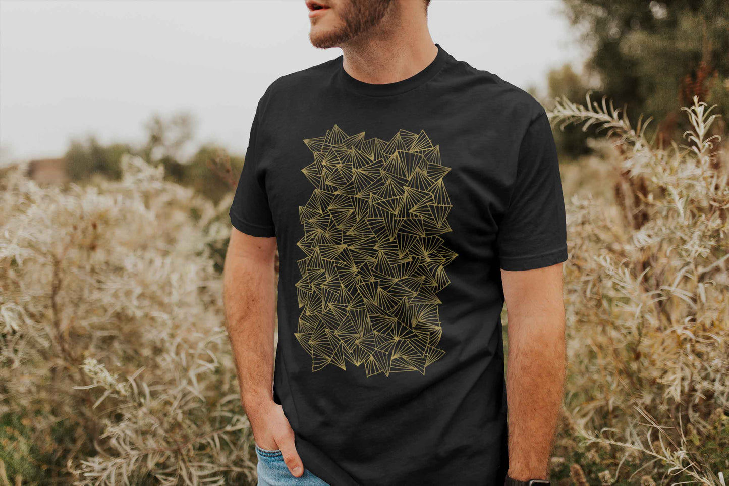 Model posing in a field with gaggle of triangles gold design on heather black unisex t-shirt.