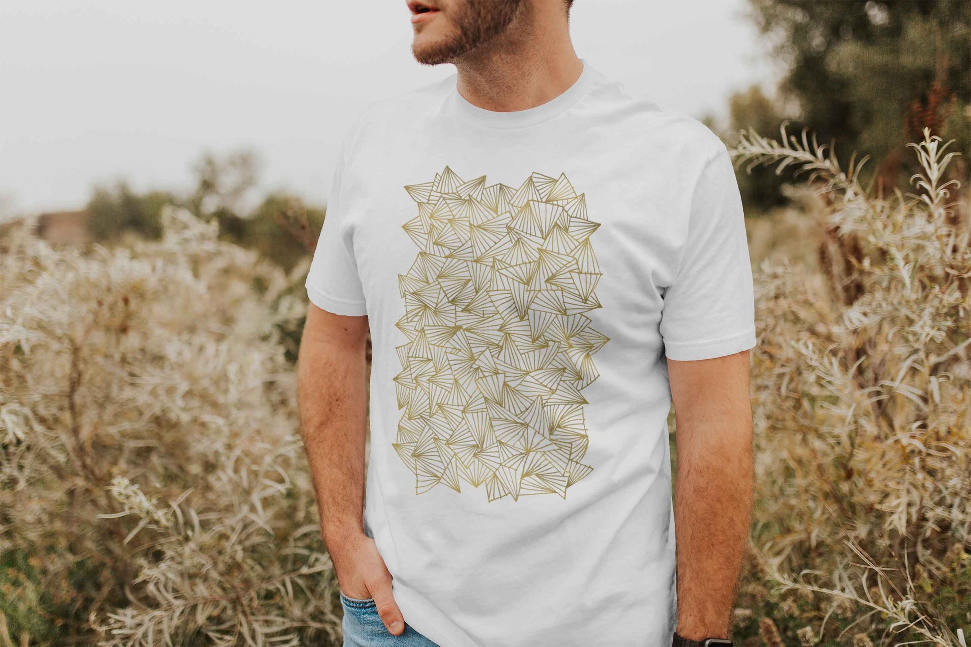 Model posing in a field with gaggle of triangles gold design on white unisex t-shirt.