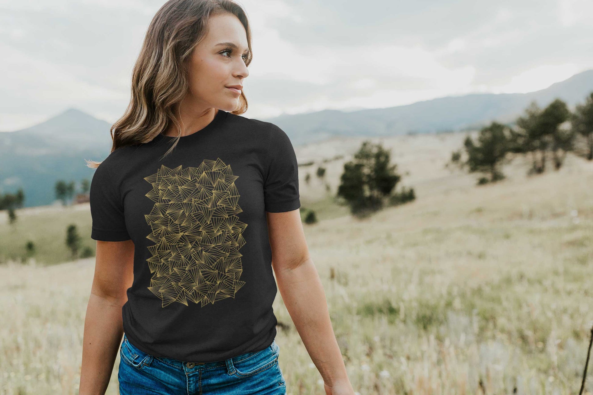 Model posing in a field with gaggle of triangles gold design on heather black unisex t-shirt.