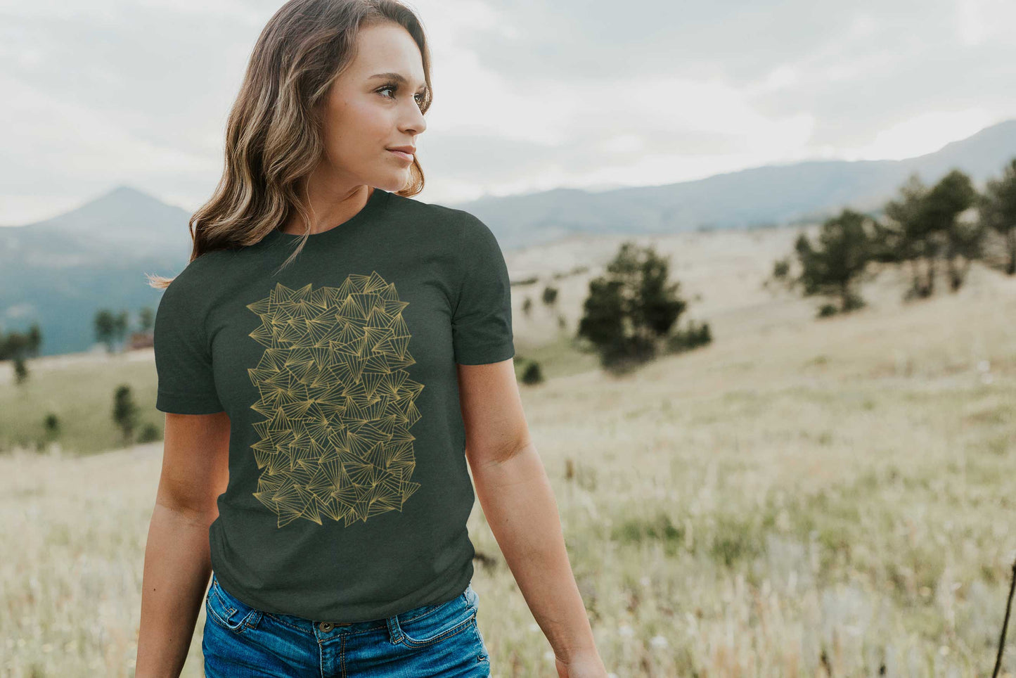 Model posing in a field with gaggle of triangles gold design on heather forest unisex t-shirt.