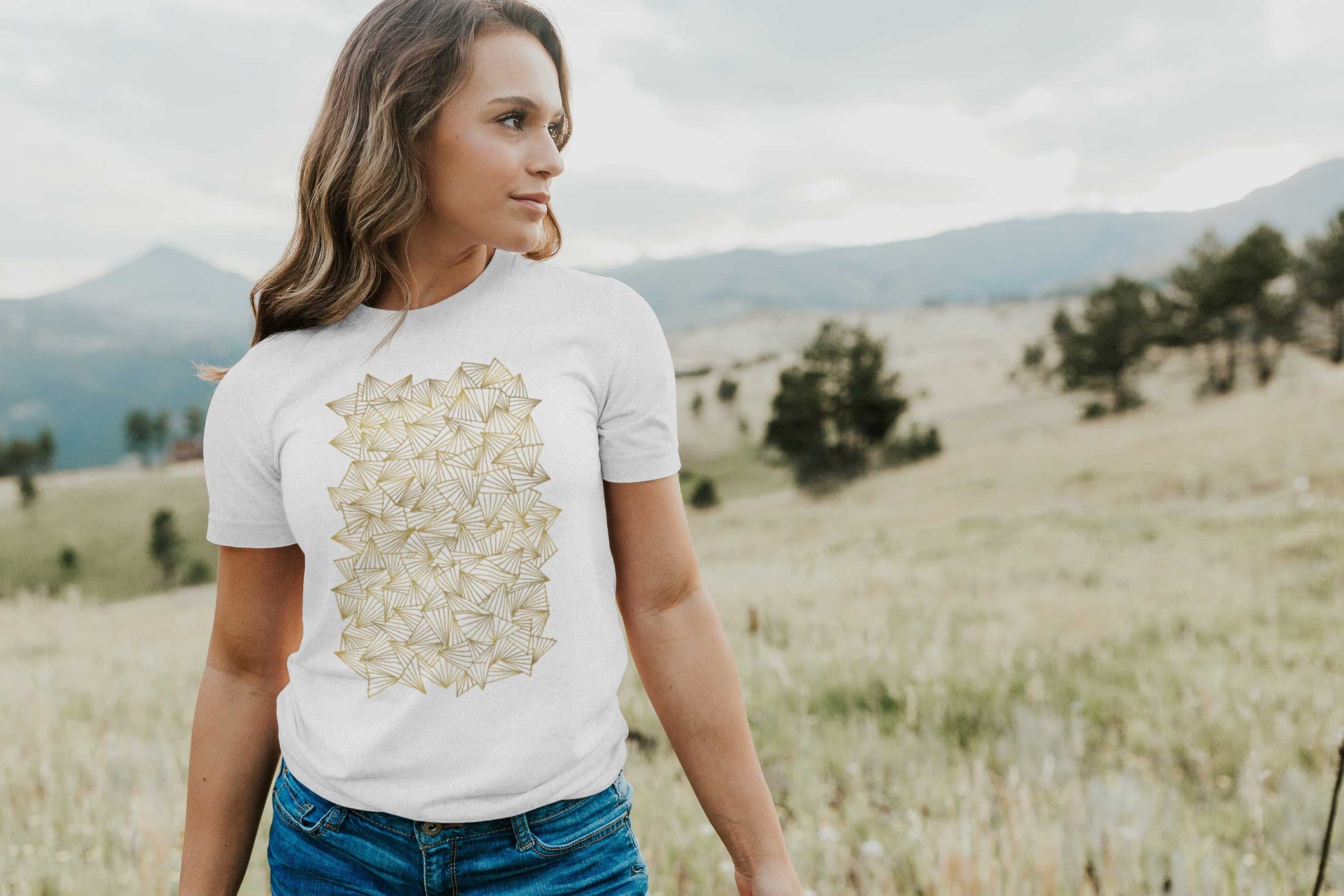 Model posing in a field with gaggle of triangles gold design on white unisex t-shirt.