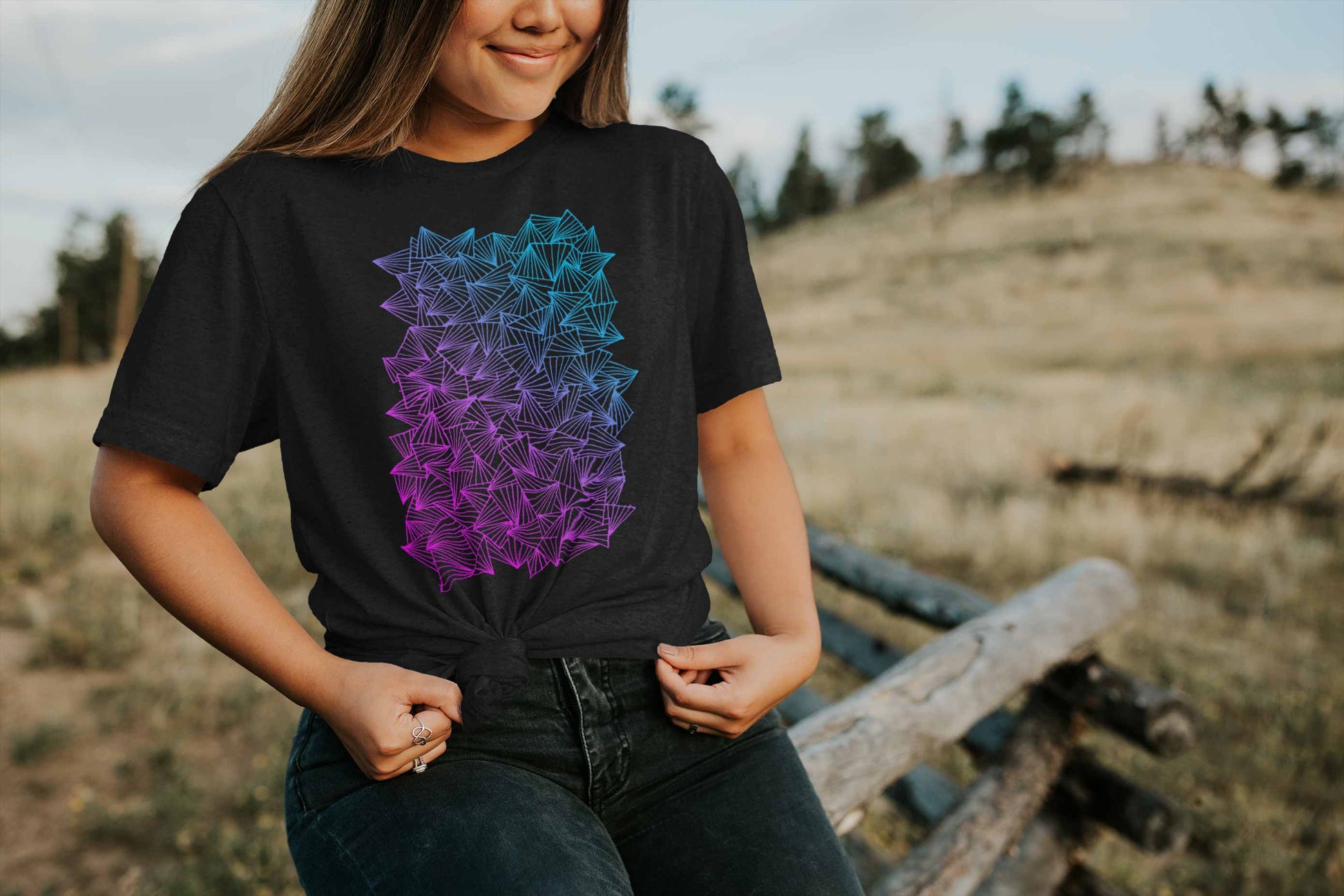 Model posing in a field with gaggle of triangles gradient design on heather black unisex t-shirt.