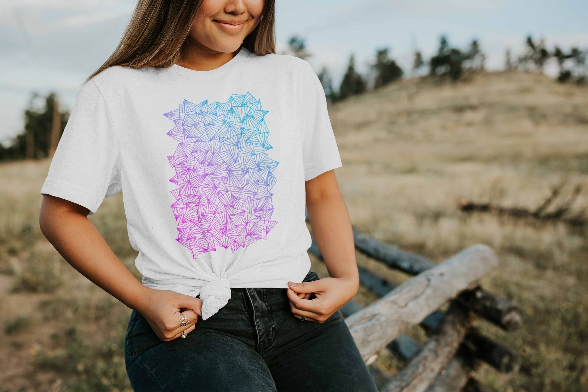 Model posing in a field with gaggle of triangles gradient design on white unisex t-shirt.