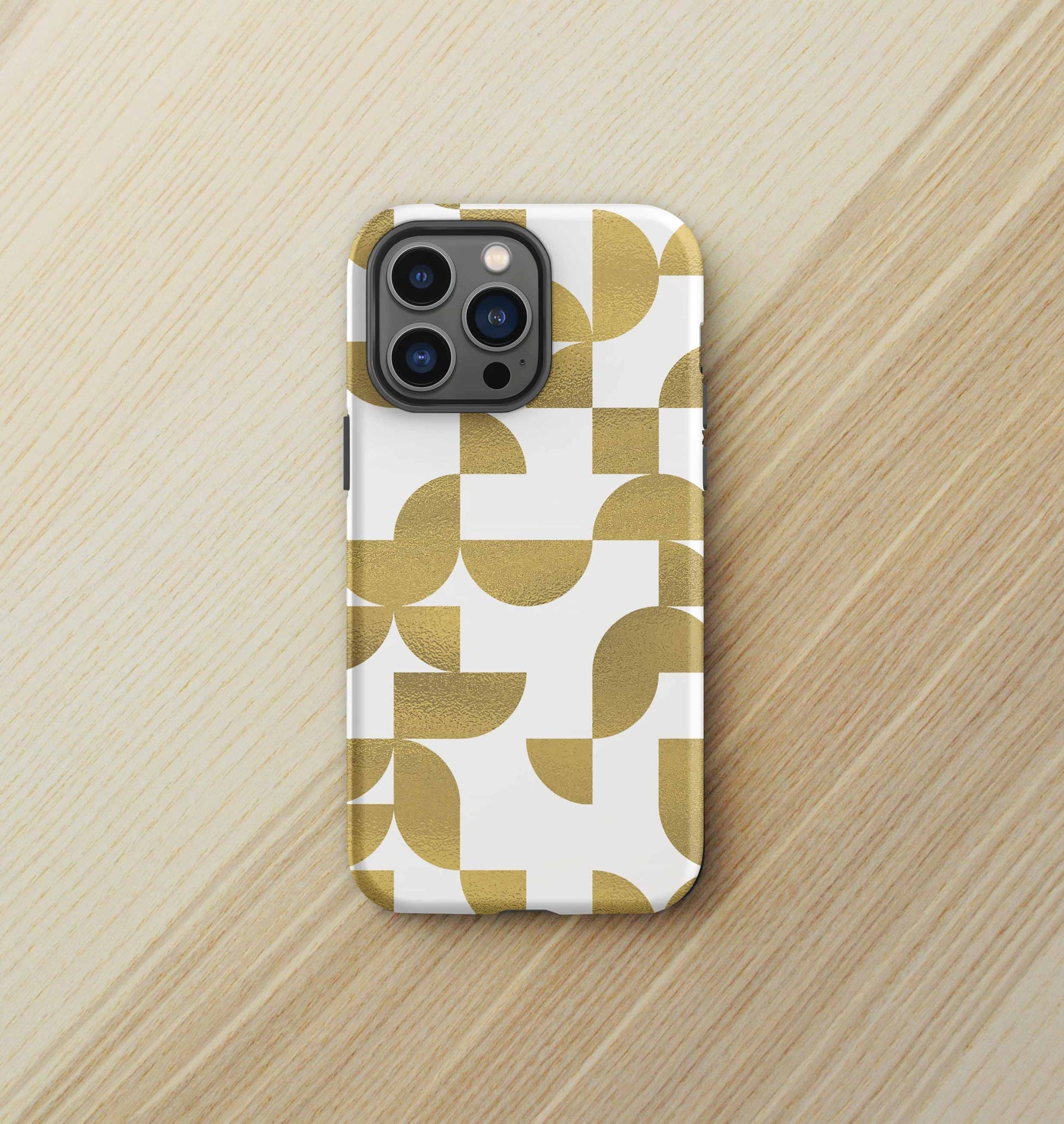 Front view of iPhone tough case in Geometria I gold design on a birch desktop