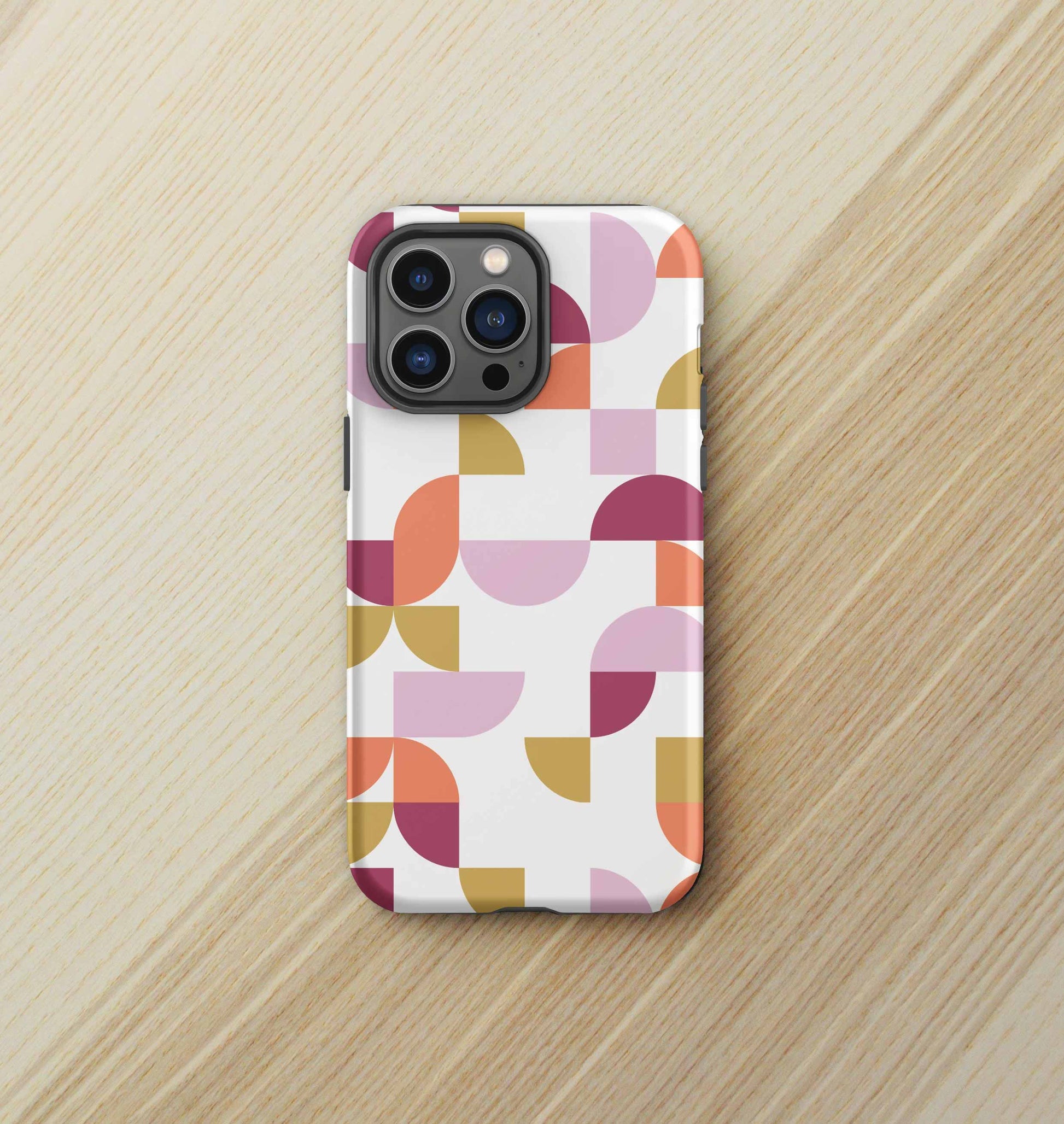 Front view of iPhone tough case in Geometria I Sunset design on a birch desktop